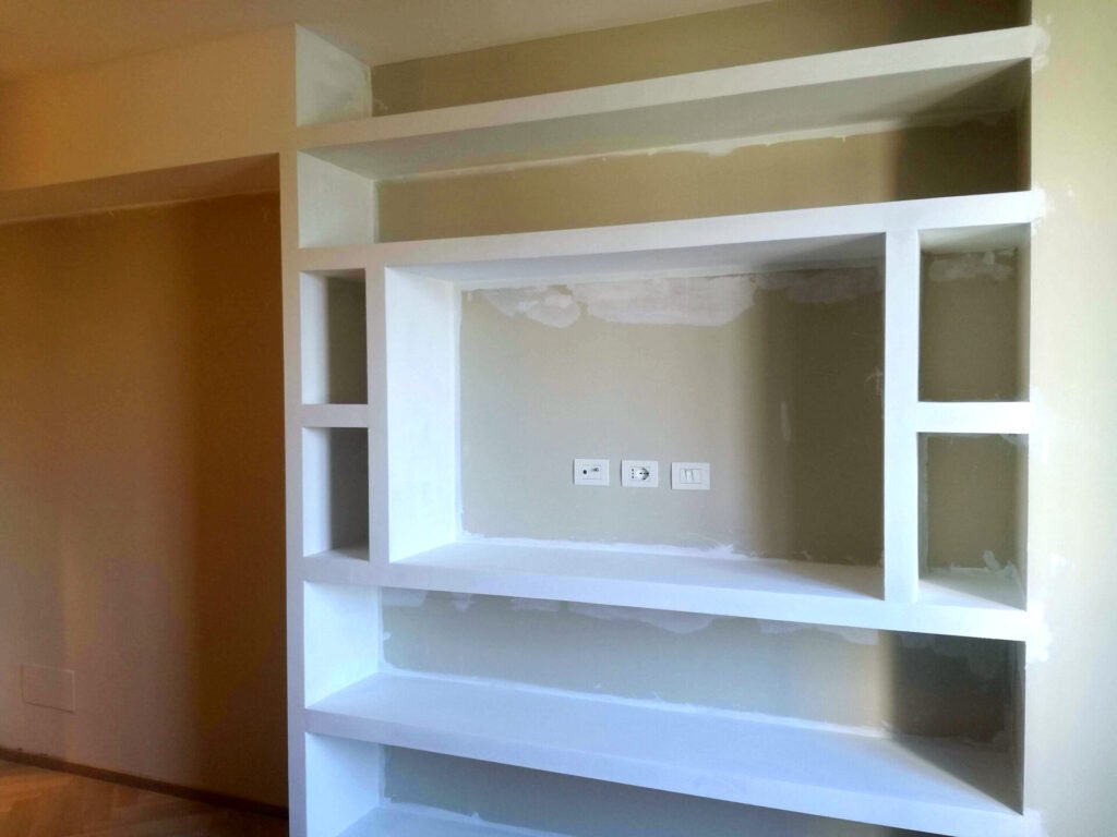 Libreria a muro in cartongesso bianco con vani aperti e ripiani, impianto elettrico visibile