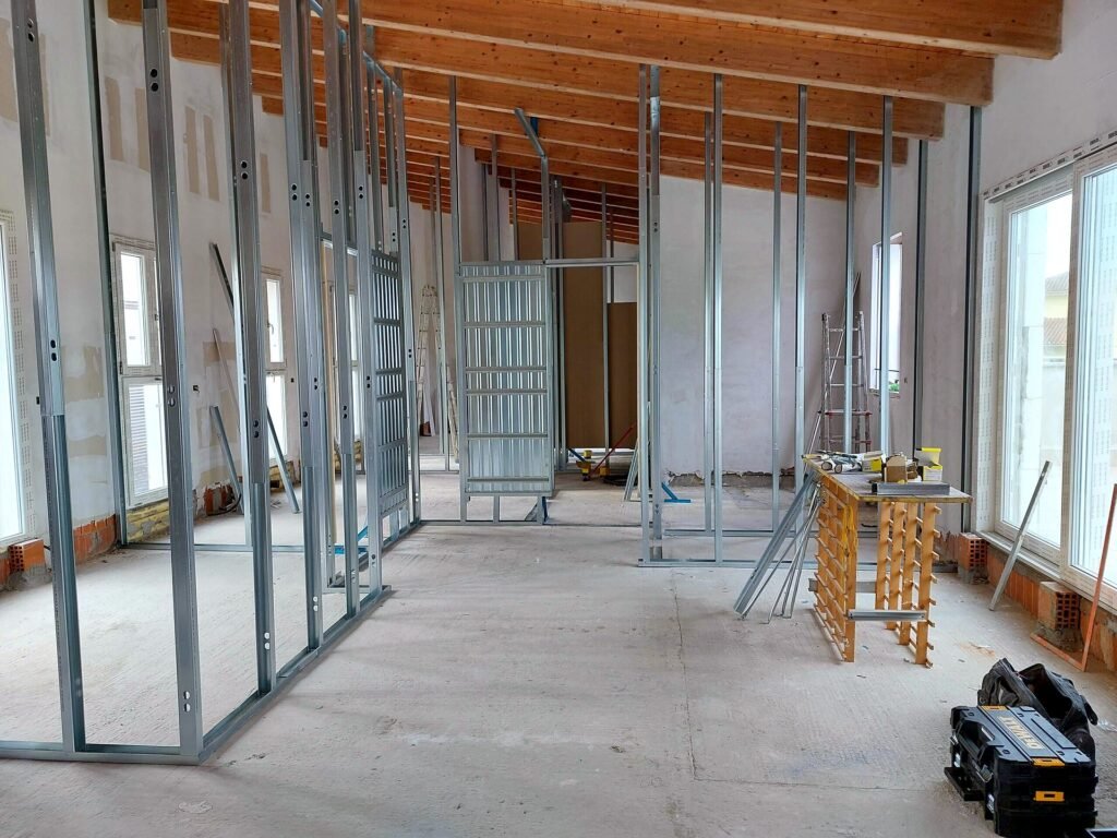 Interno in costruzione con struttura in cartongesso e infissi in alluminio, pavimento grezzo e travi in legno a vista
