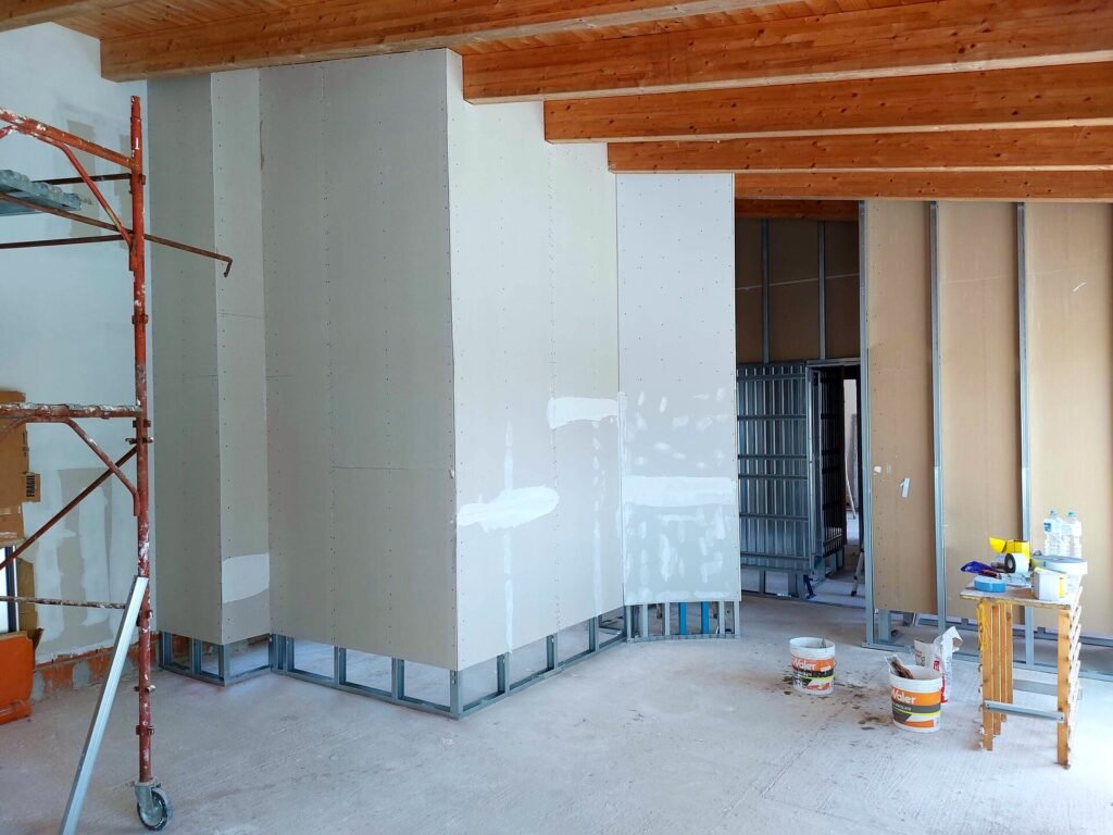 Interno in costruzione con pareti in cartongesso, travi in legno a vista e impianti in corso di realizzazione