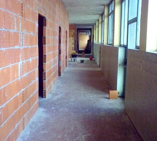 Corridoio in fase di ristrutturazione con pareti in laterizio rosso e pavimento grigio
