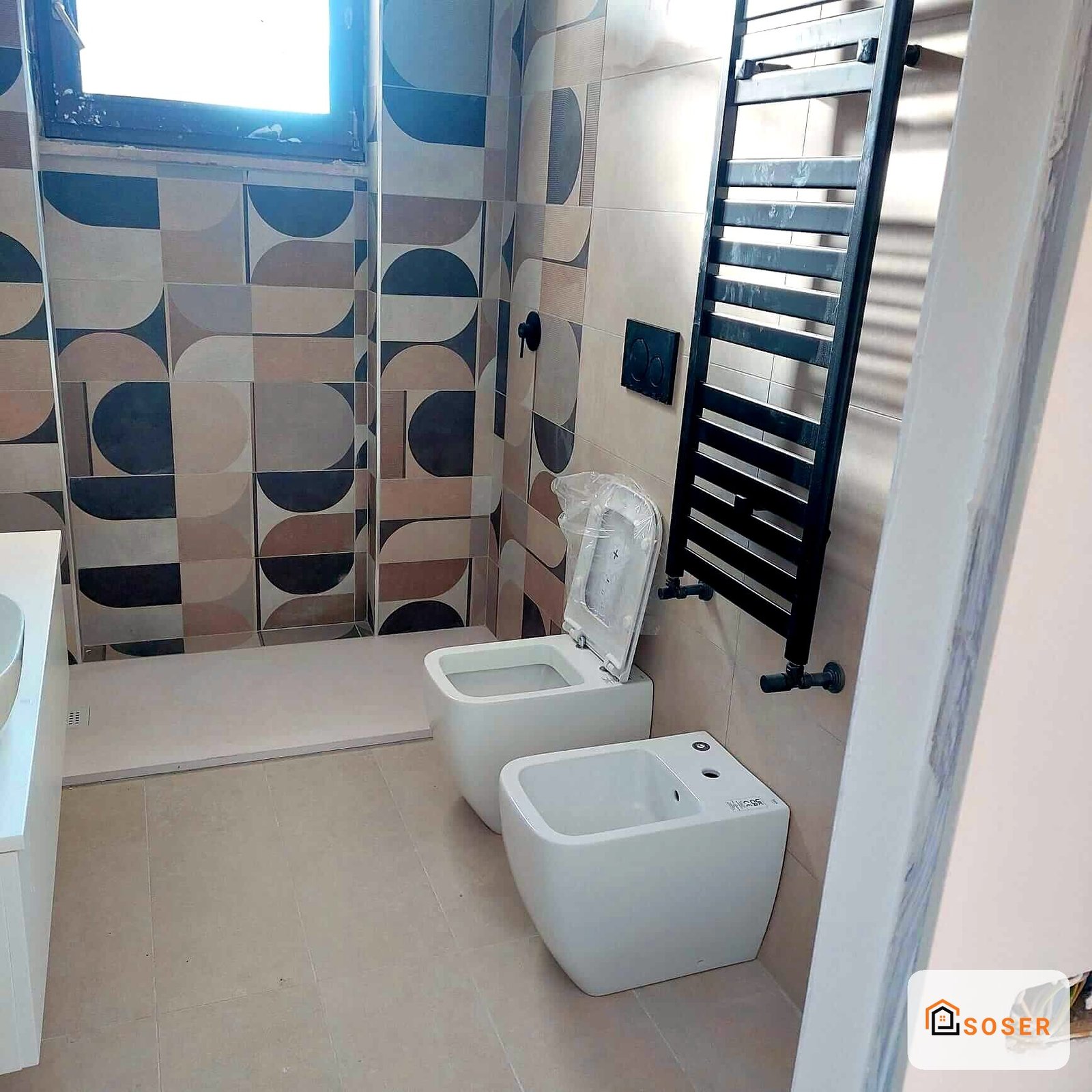 Bagno in ristrutturazione con piastrelle geometriche blu e beige, sanitari bianchi e scaldasalviette nero