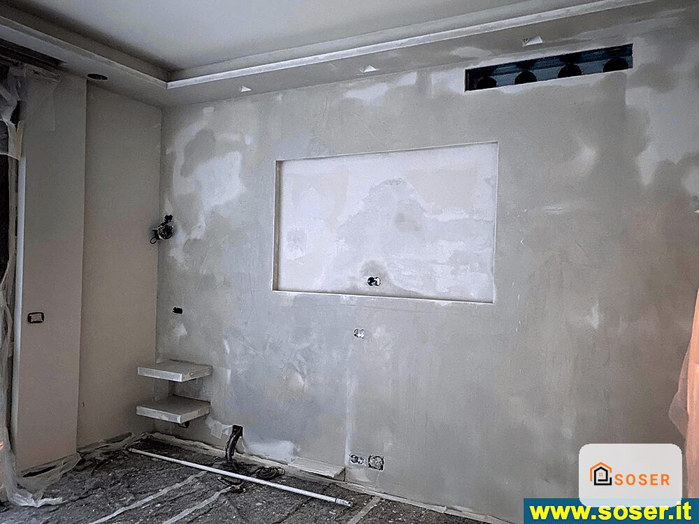 Camera in corso di ristrutturazione con pareti in cartongesso, finestra e impianti elettrici visibili