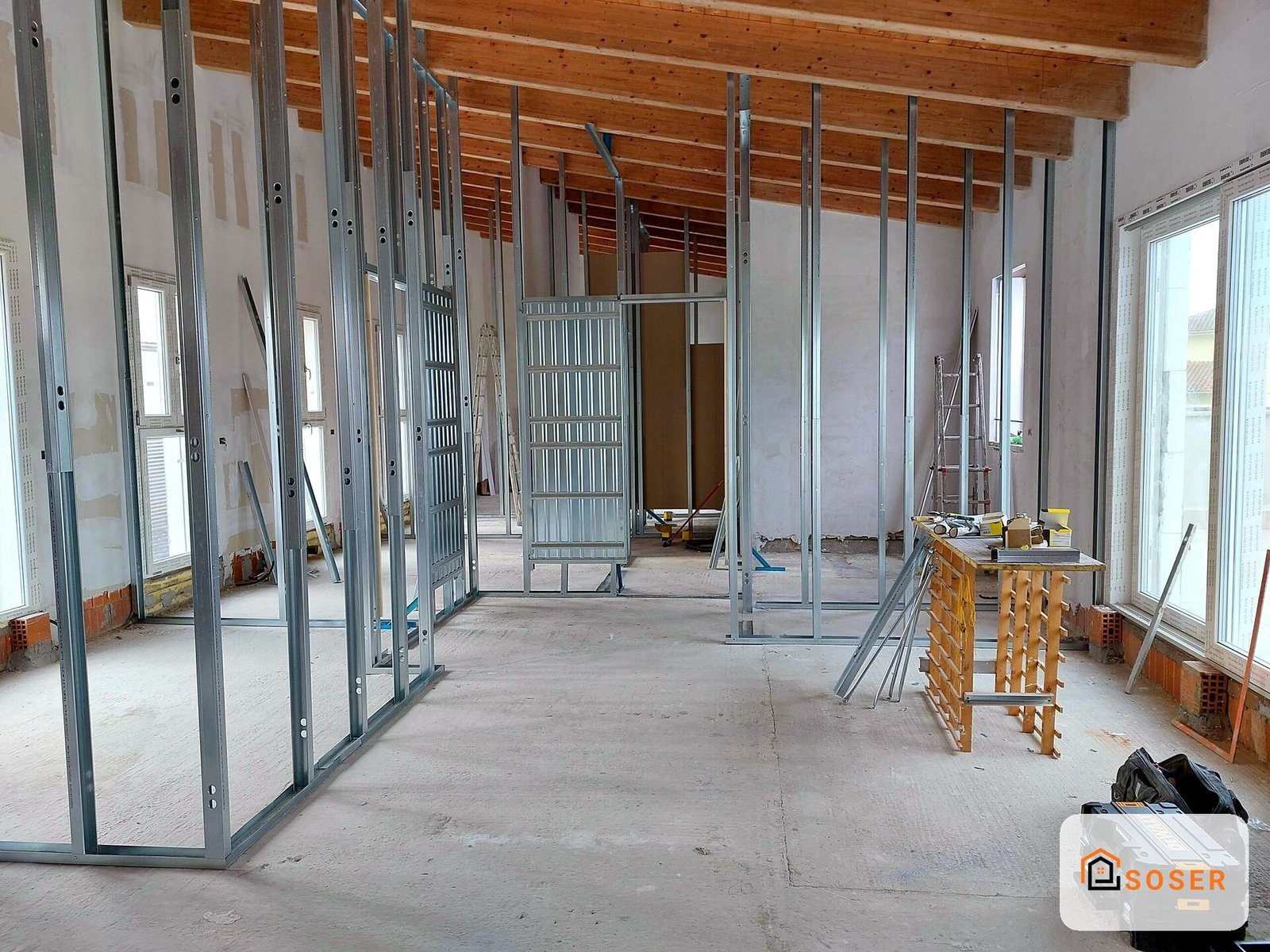 Interno in costruzione con struttura in cartongesso e infissi in alluminio, pavimento grezzo e travi in legno a vista