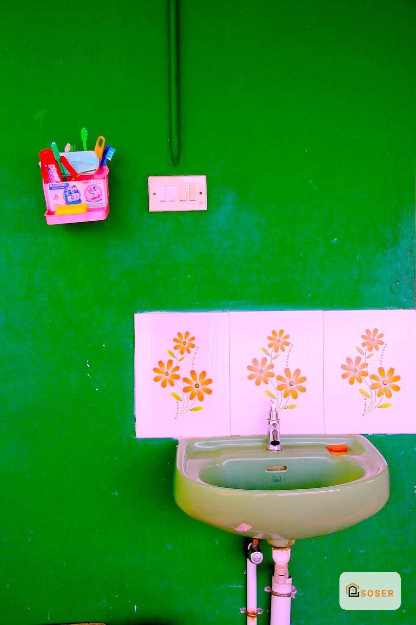 Bagno con parete verde brillante, lavabo bianco e specchio decorato con fiori gialli