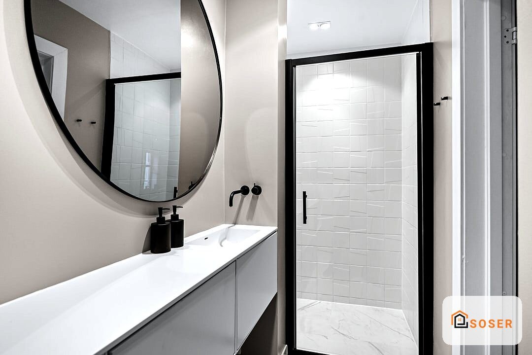 Bagno moderno con lavabo bianco, specchio rotondo nero e doccia con piastrelle bianche