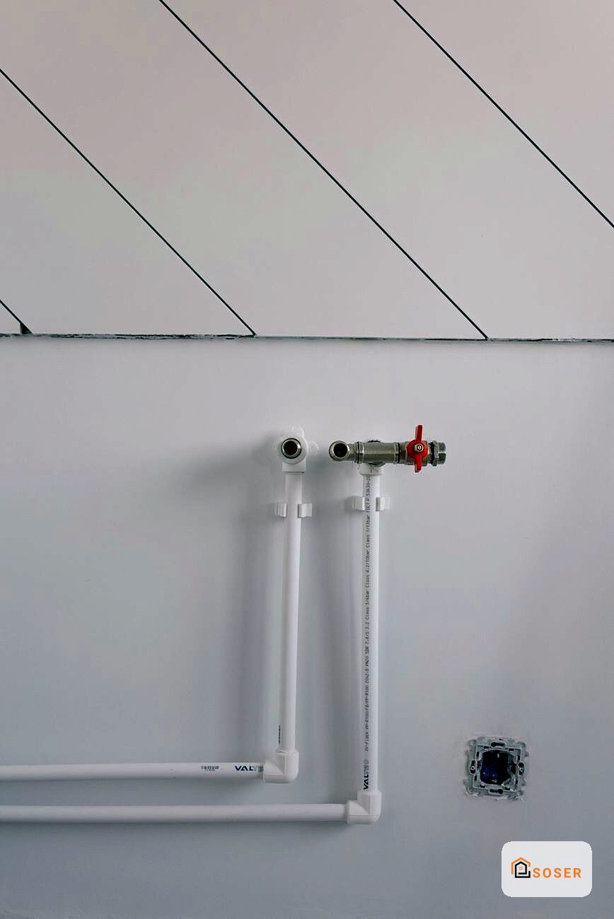 Impianto idraulico a parete con tubi bianchi, valvola rossa e scatola elettrica su muro grigio con divisori in cartongesso