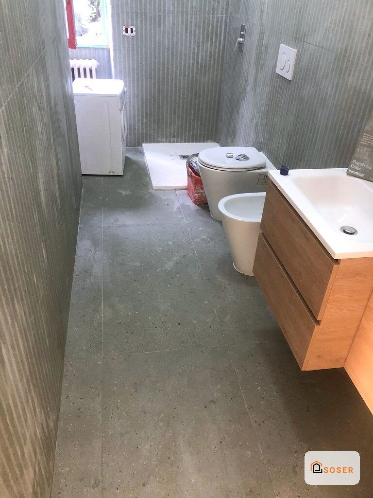 Bagno in fase di ristrutturazione con pavimento in cemento grigio e sanitari installati