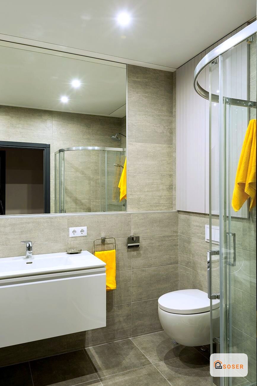 Bagno moderno con rivestimento in travertino beige, sanitari bianchi e dettagli gialli a Milano