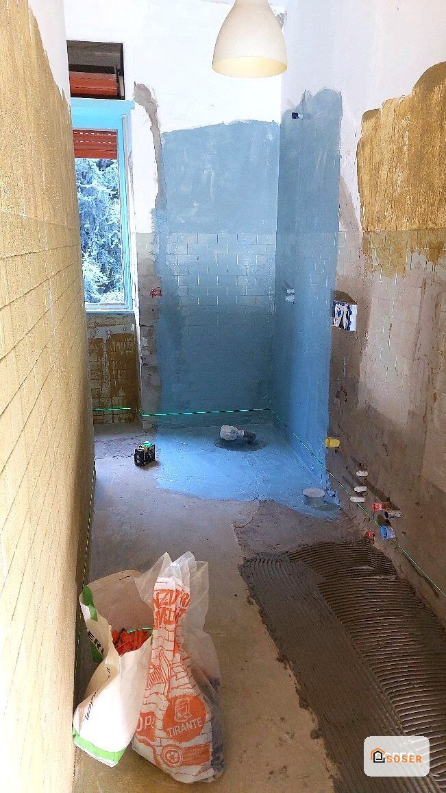 Bagno in ristrutturazione con pareti in piastrelle blu e gialle, pavimento in cemento e materiali da costruzione