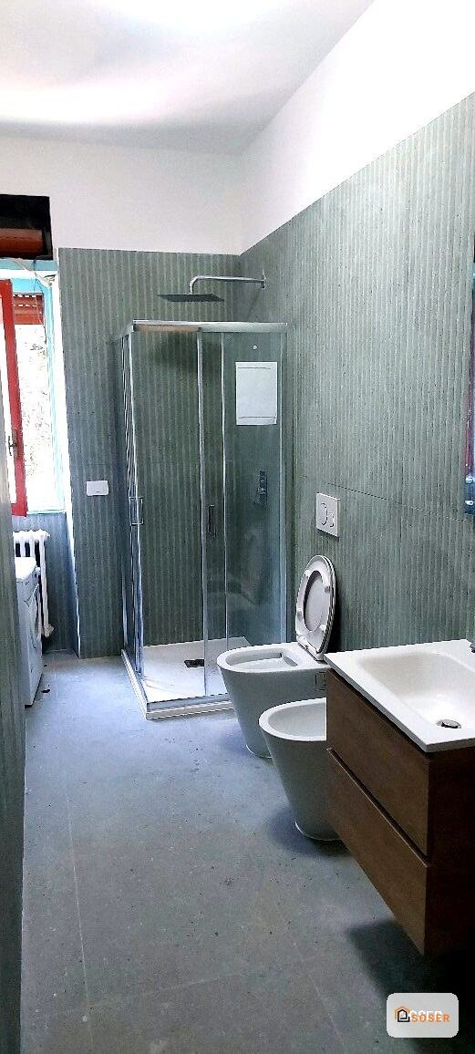 Bagno in ristrutturazione con piastrelle grigie, sanitari bianchi e rivestimenti in corso di lavoro