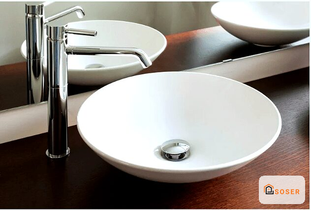 Lavabo rotondo bianco in ceramica con miscelatore cromato su piano in legno scuro