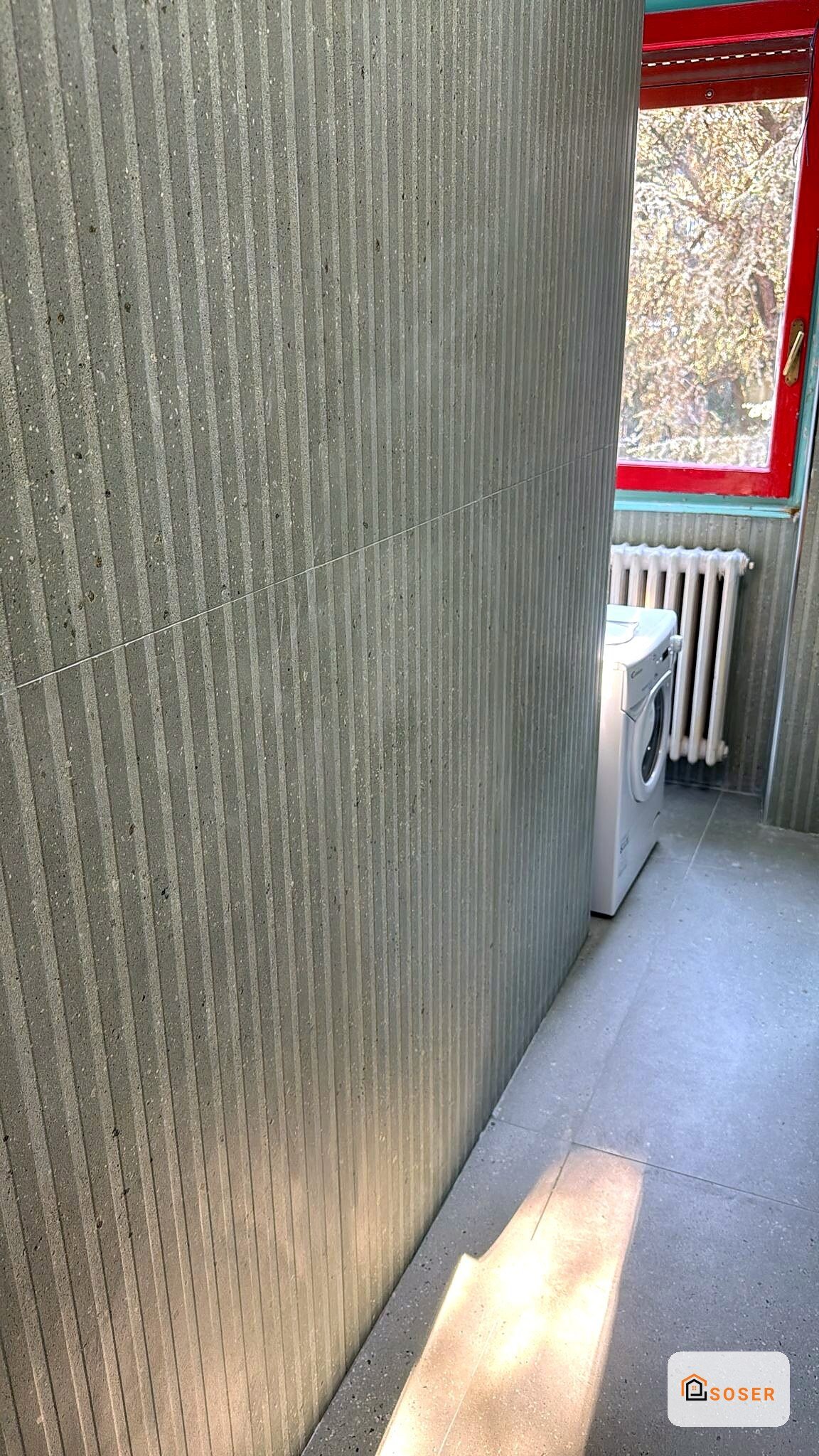Corridoio con pareti in cemento grigio e radiatore bianco, finestra con infisso rosso