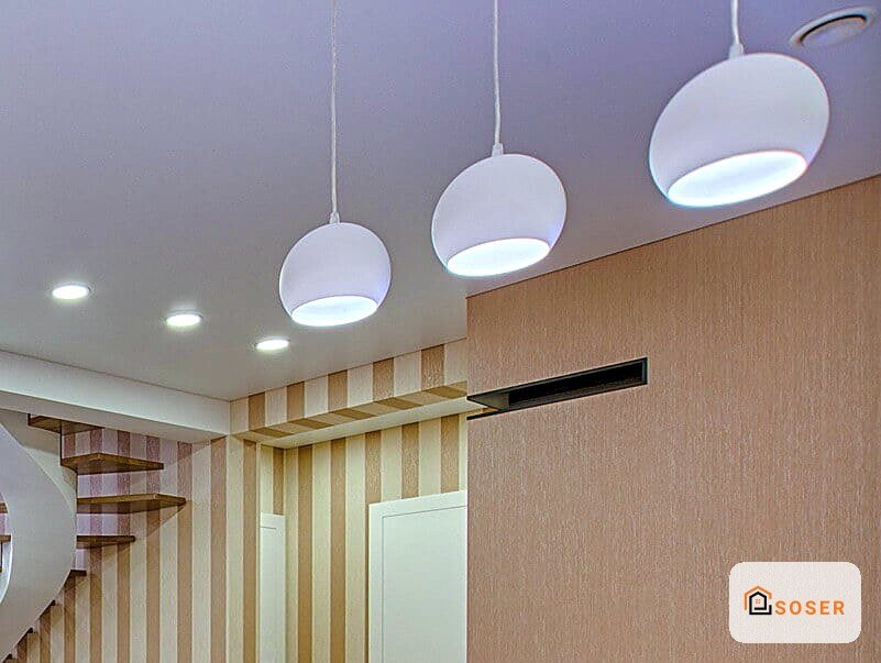 Soffitto in cartongesso bianco con tre lampadari pendenti sferici e parete rivestita in carta da parati a righe beige e bianche