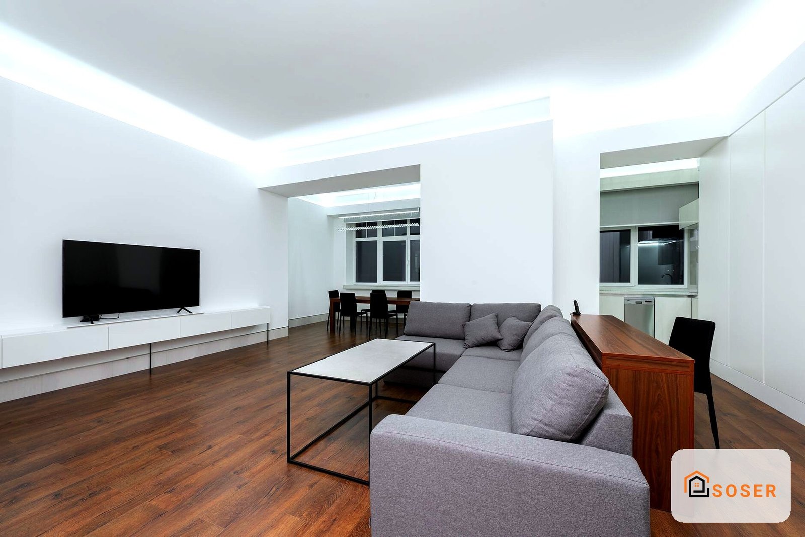 Soggiorno moderno con pavimento in legno, divano grigio e TV su parete bianca, illuminazione a LED