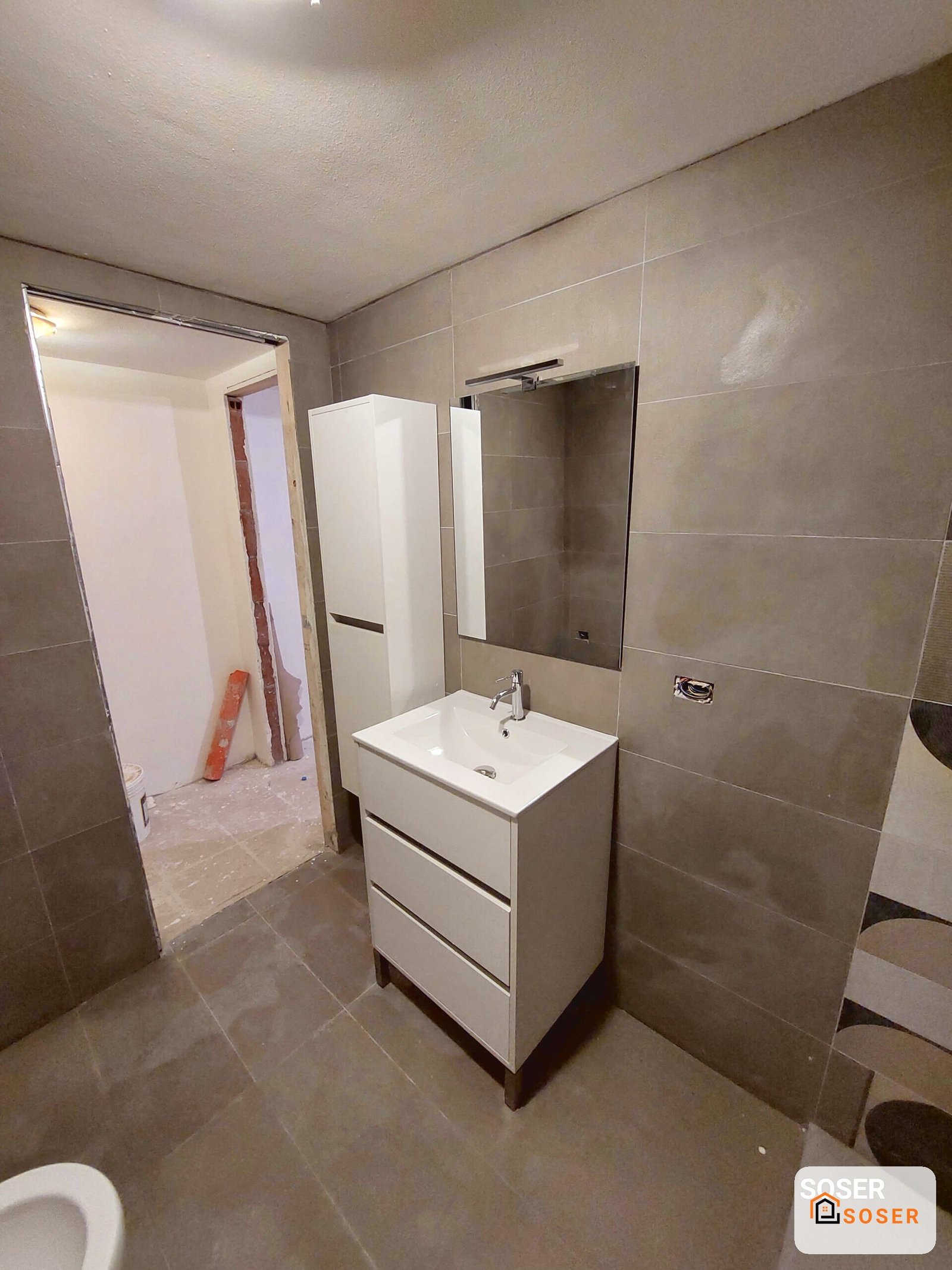 Bagno moderno in fase di ristrutturazione con lavabo bianco e piastrelle grigie