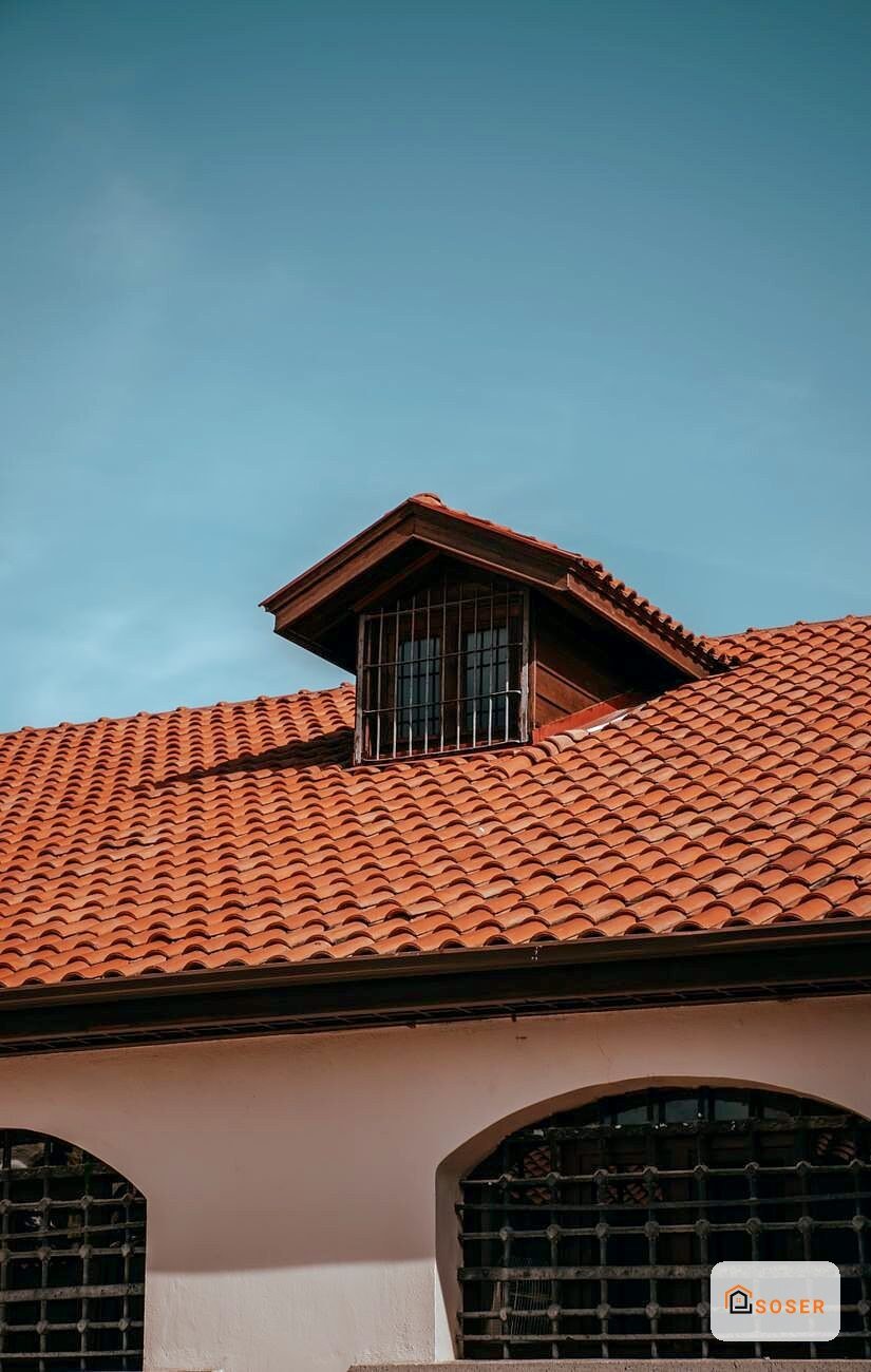 Tetto con coppi in terracotta e finestra di mansarda con grate metalliche su facciata rosa