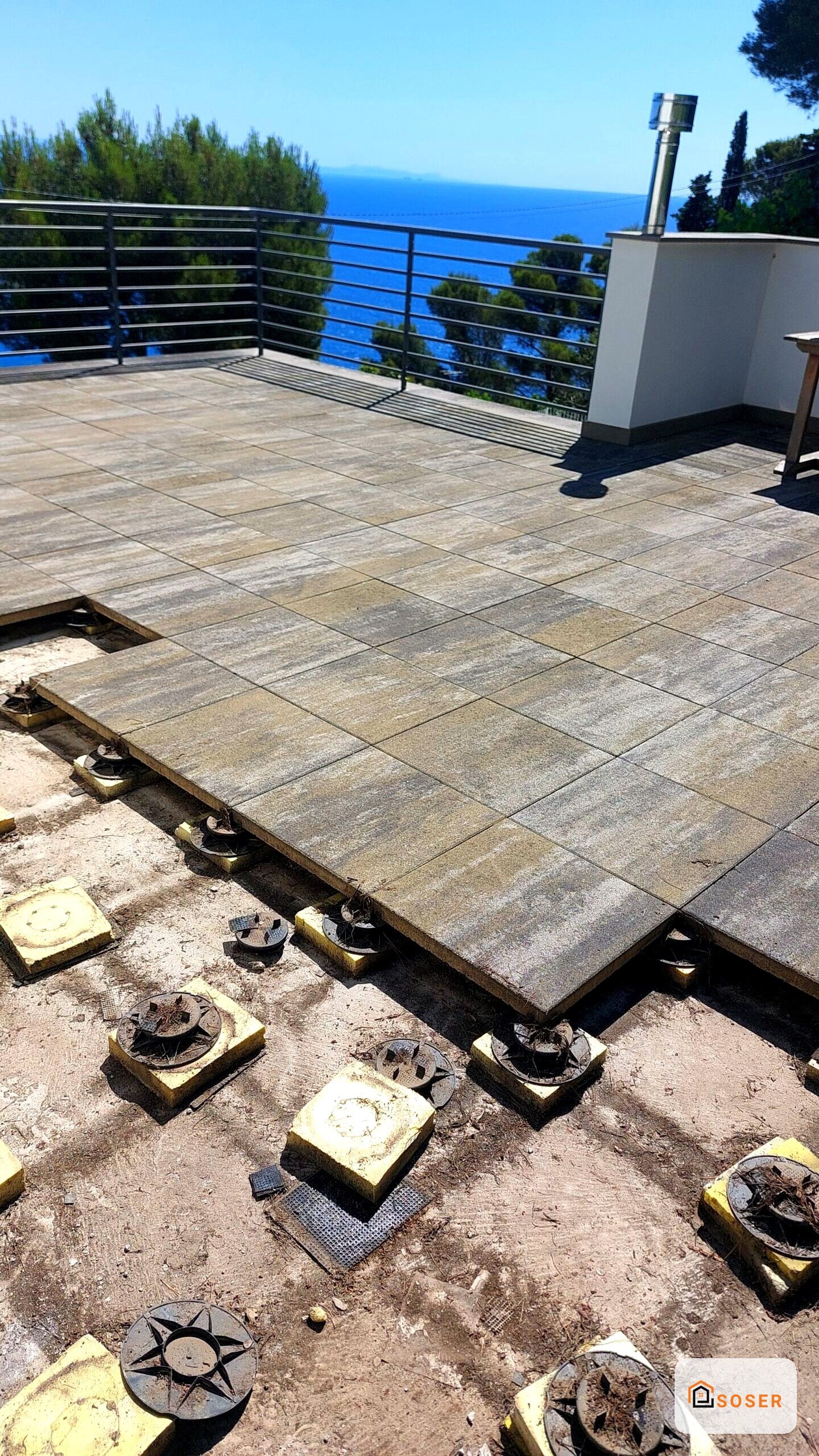 Terrazza con pavimentazione in corso di posa e vista panoramica sul mare, supporti di livellamento visibili