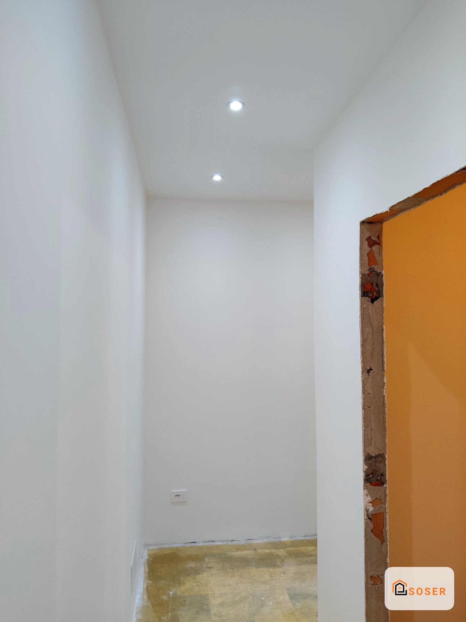 Corridoio stretto in fase di ristrutturazione con pareti in cartongesso bianco e porta arancione