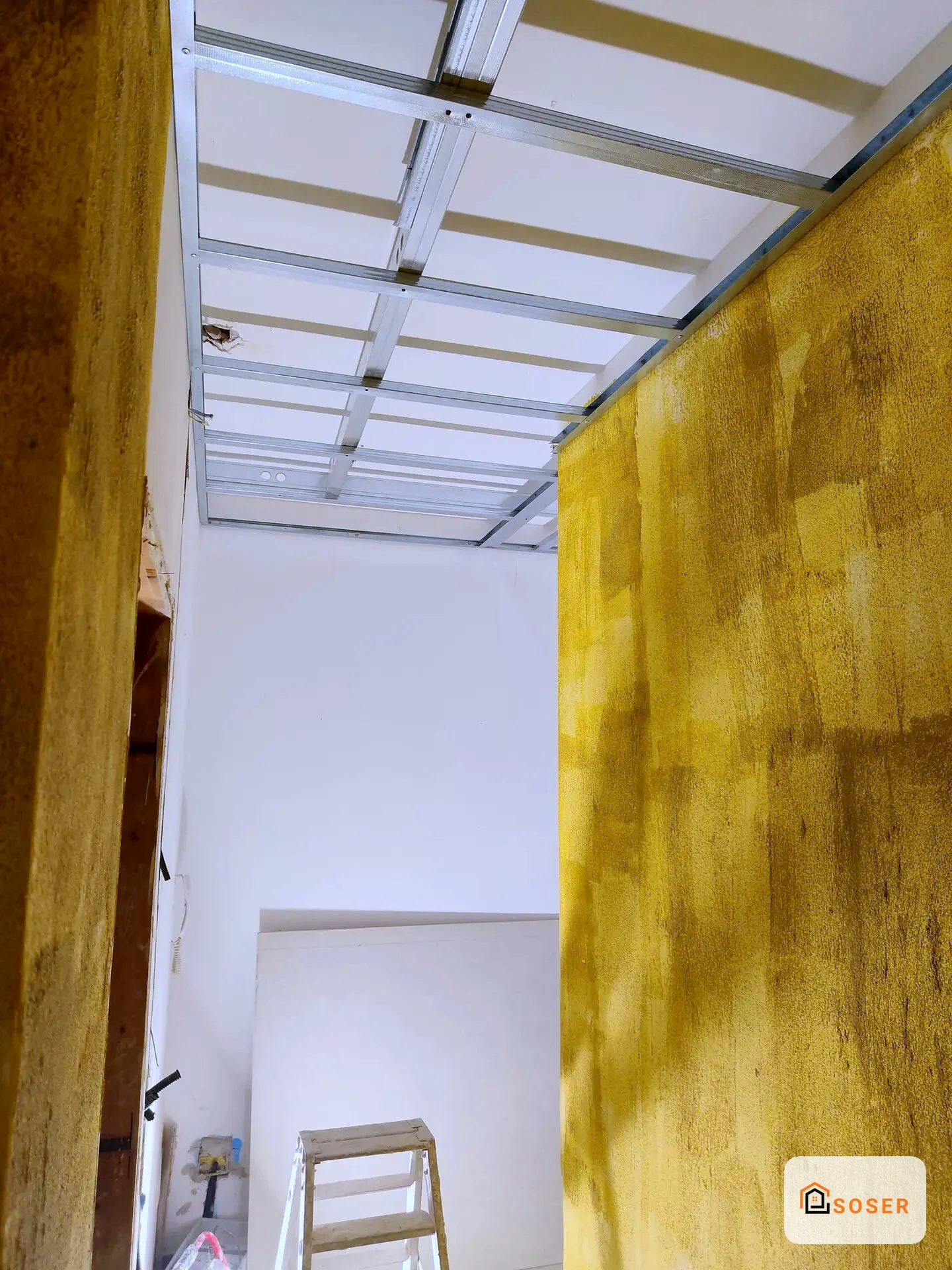 Corridoio in ristrutturazione con pareti in cartongesso giallo e controsoffitto in alluminio a Milano