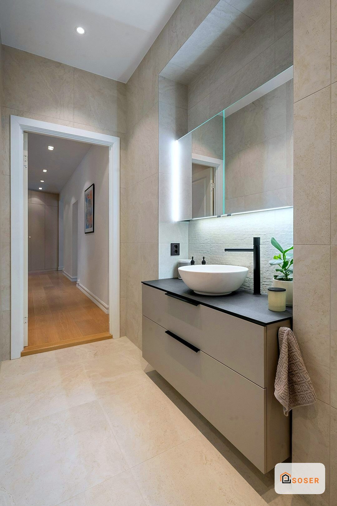 Bagno moderno con lavabo rotondo bianco, specchio illuminato e rivestimenti in travertino beige