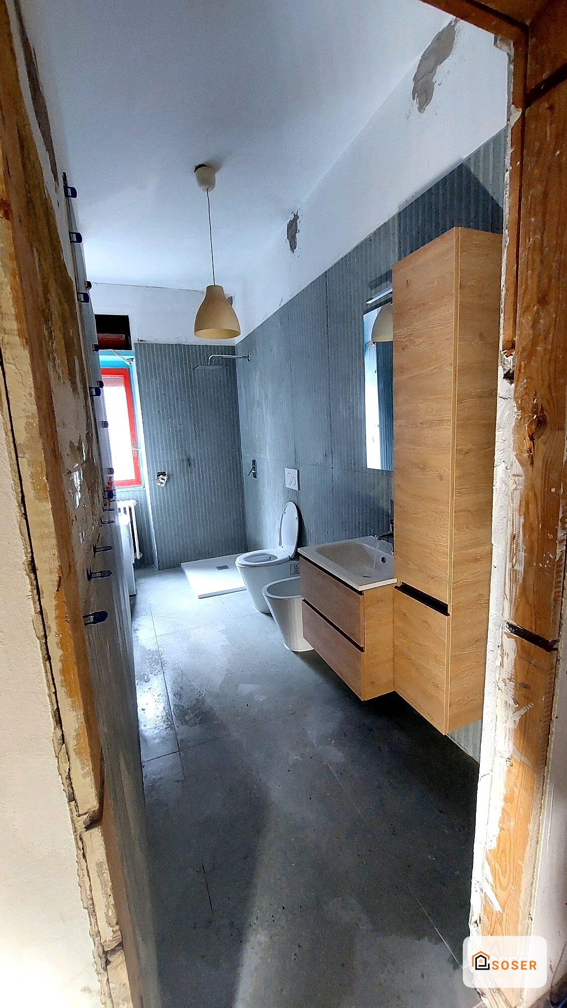Bagno in ristrutturazione con vanità in legno, rivestimento grigio e pavimento in cemento