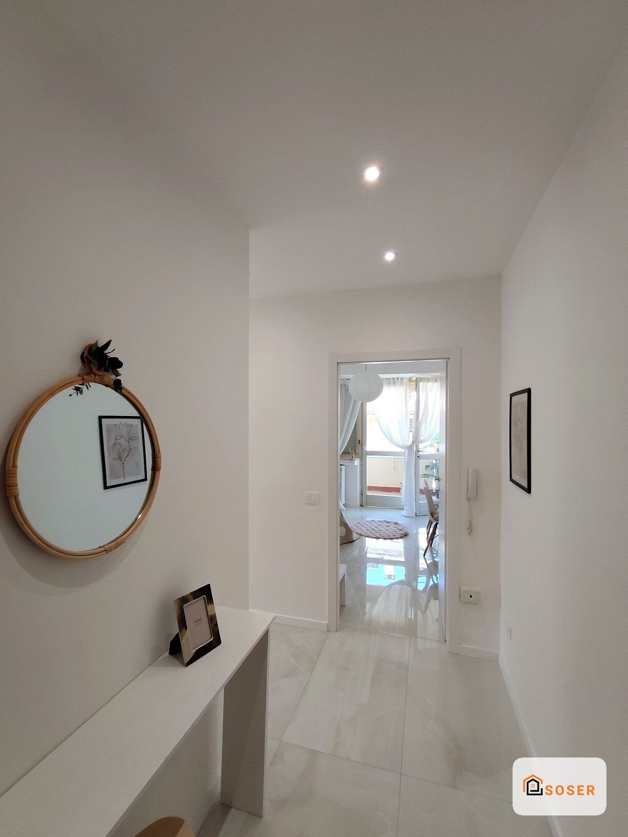 Corridoio moderno con pavimenti in marmo bianco, specchio rotondo in legno e porta vetrata che accede al soggiorno