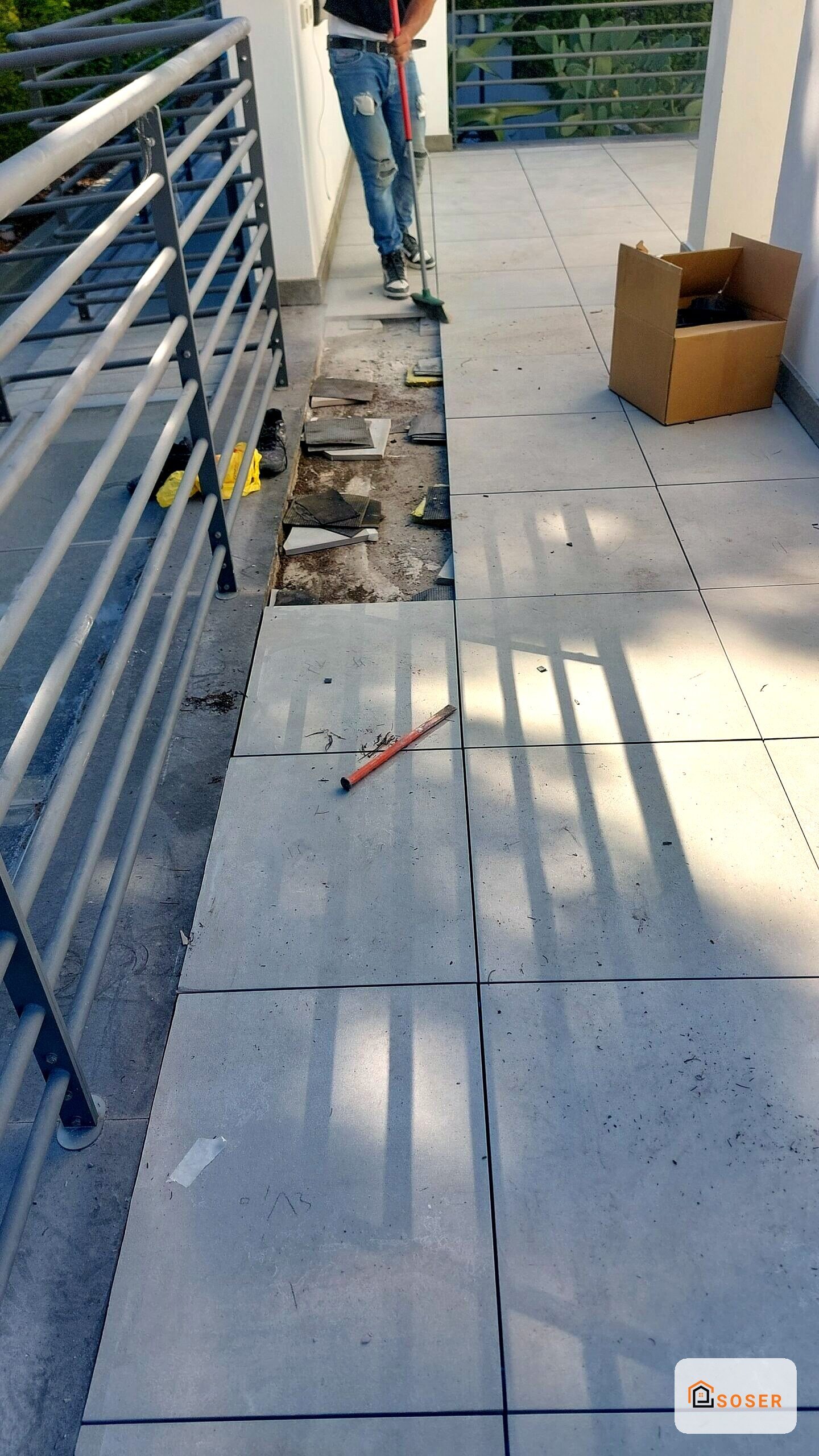 Posa di piastrelle in cemento su terrazza esterna durante ristrutturazione, con attrezzi da lavoro