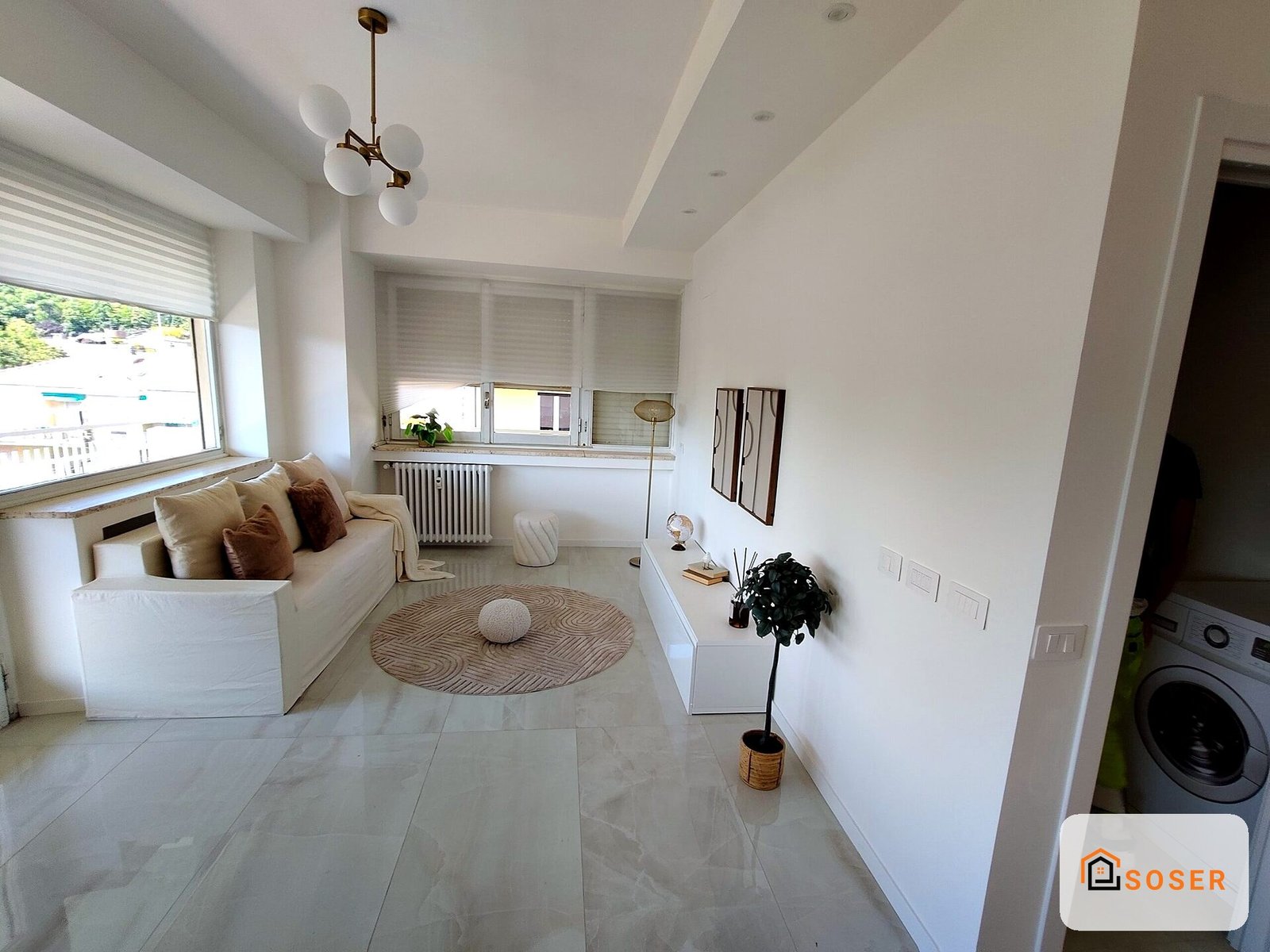 Soggiorno moderno luminoso con pavimenti in marmo bianco, divano beige e finestre con veneziane