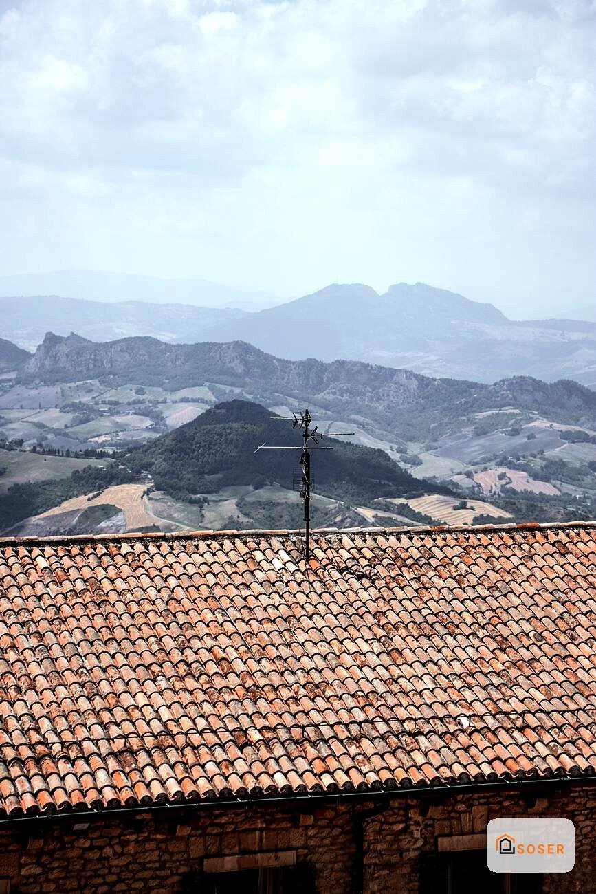 Tetto in coppi tradizionali con antenna su casa rurale, paesaggio toscano sullo sfondo