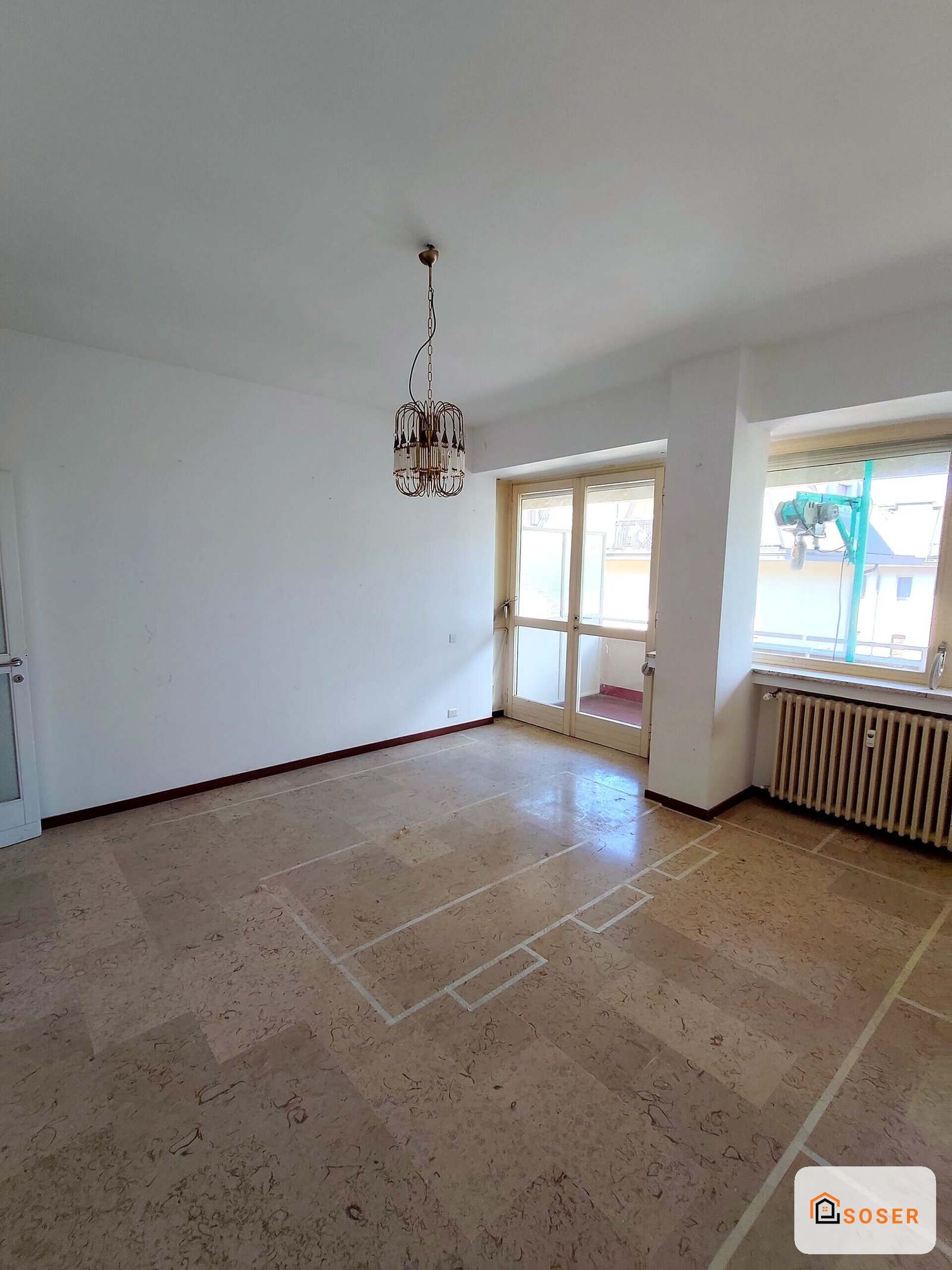 Soggiorno vuoto con pavimento in cotto e balcone, prima della ristrutturazione