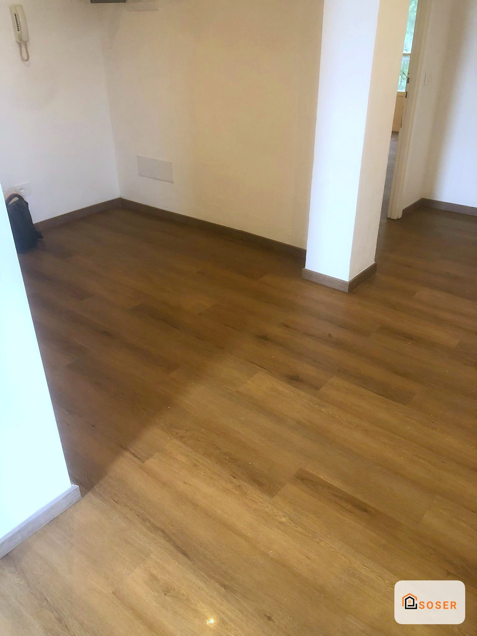 Pavimento in legno scuro in ampia stanza con pareti chiare e colonne bianche