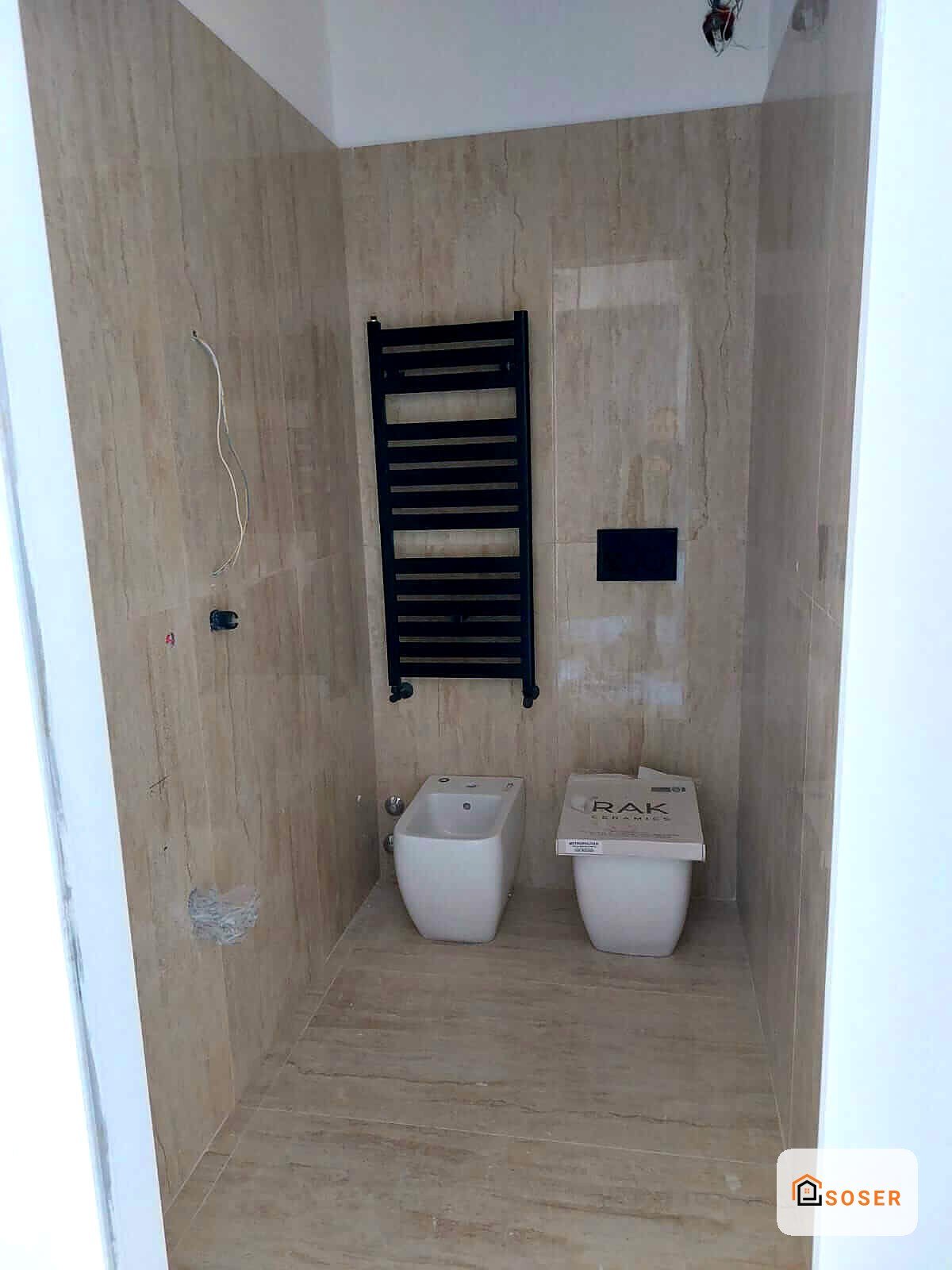 Bagno in ristrutturazione con piastrelle in stile legno, scaldasalviette nero e due sanitari bianchi