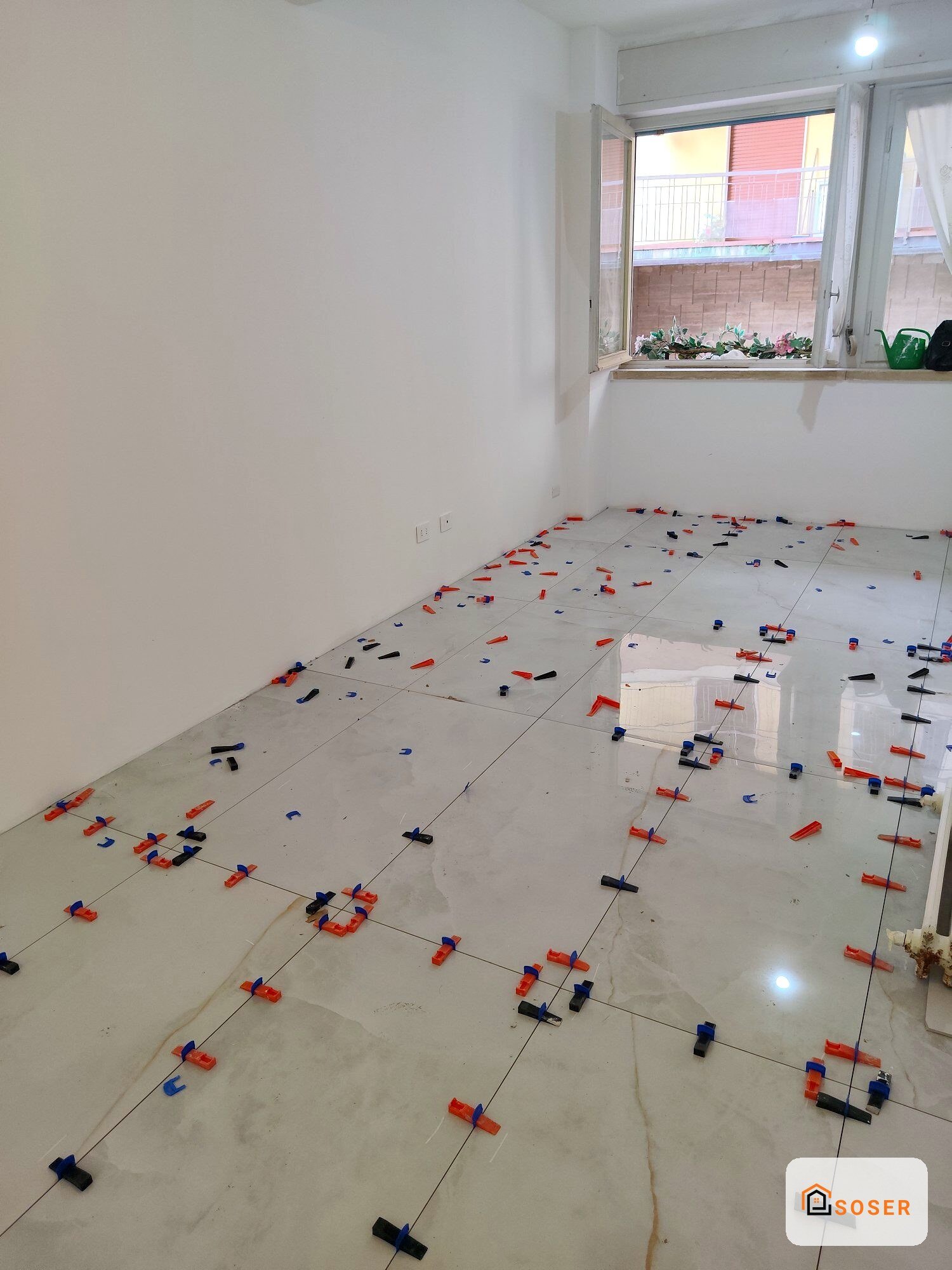 Posa di piastrelle in ceramica con distanziatori rossi e blu su pavimento in una stanza vuota