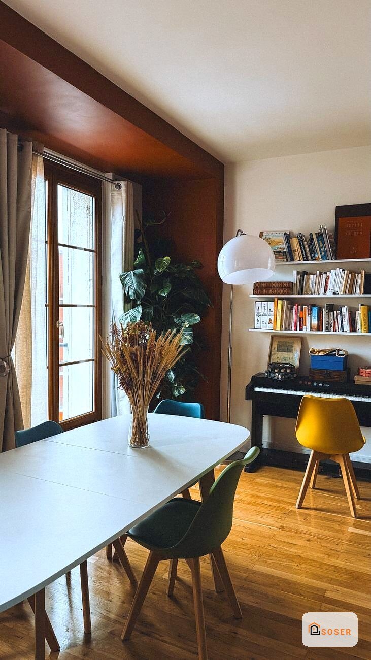 Sala da pranzo moderna con tavolo bianco, sedie nere, parete marrone e libreria, infissi in legno