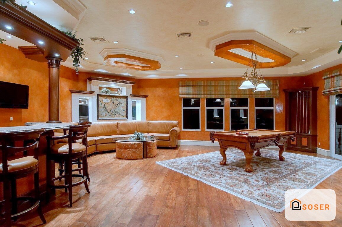 Sala giochi lussuosa con pareti arancioni, pavimenti in legno, tavolo da biliardo e arredamento in legno scuro