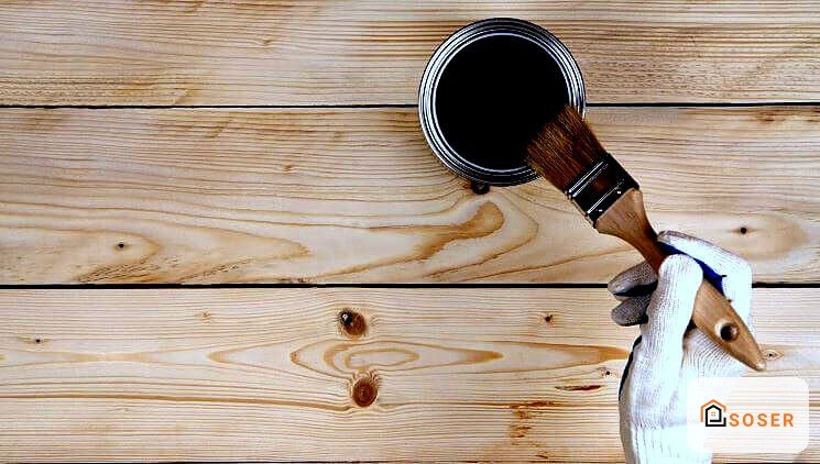 Mano applica vernice scura su pavimento in legno durante lavori di ristrutturazione