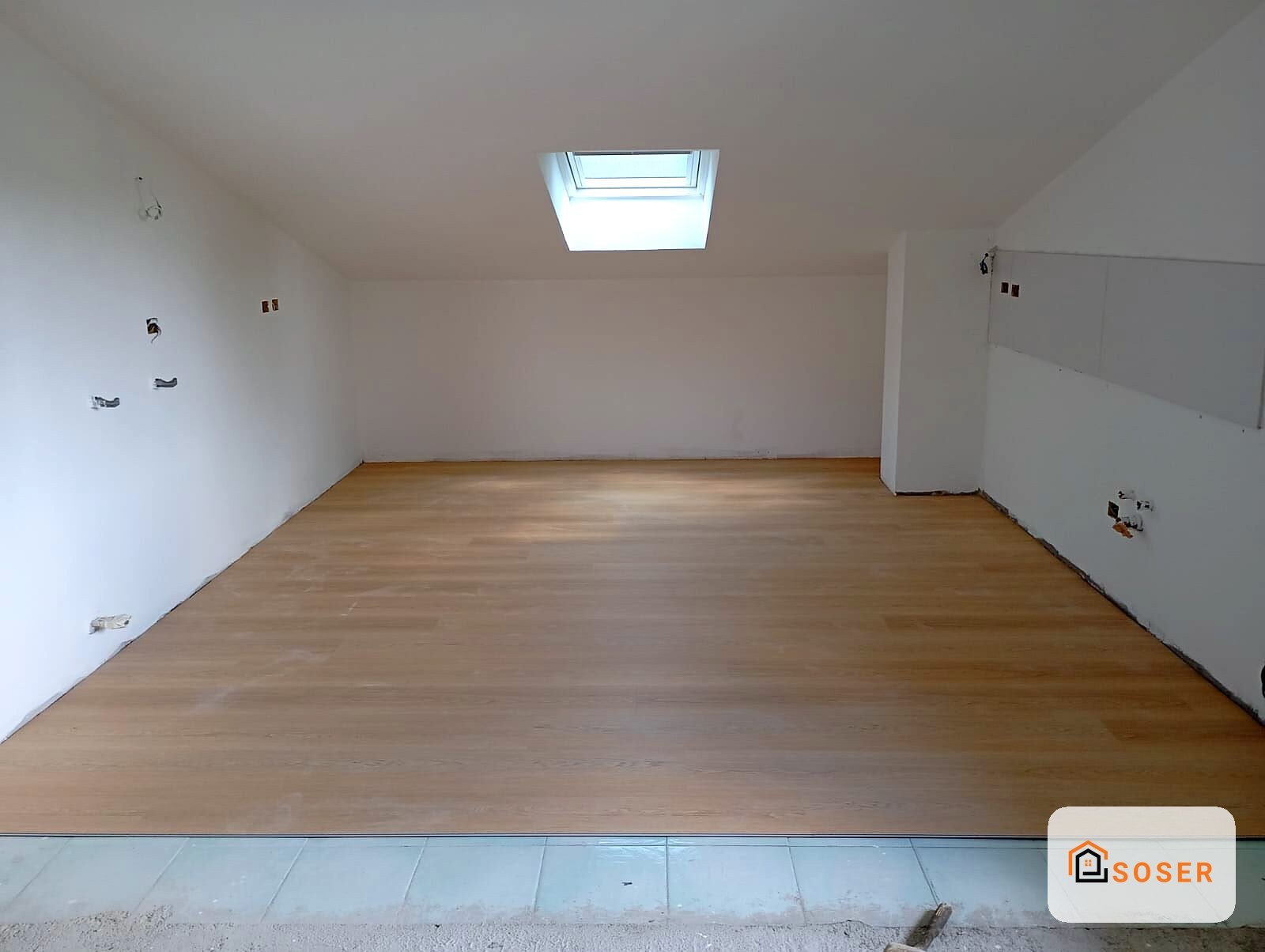 Sottotetto con pavimento in legno, pareti bianche e lucernario, pronto per la finitura