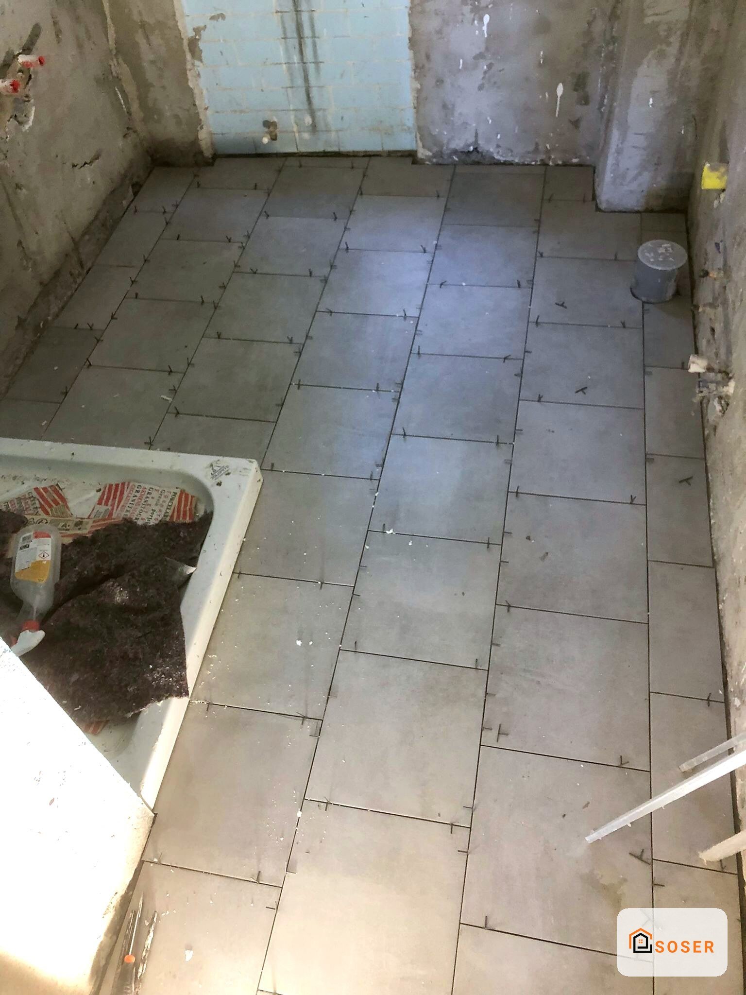Bagno in ristrutturazione con piastrelle in corso di posa su pavimento grigio