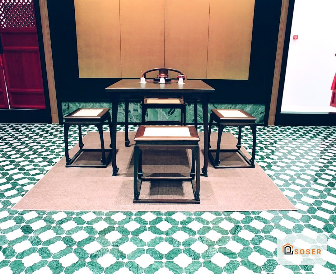 Showroom di pavimenti con piastrelle geometriche verdi e bianche, tavoli espositivi e grande schermo