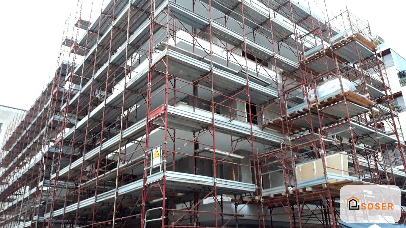 Edificio in costruzione con ponteggi rossi e impalcature metalliche, struttura in cemento armato con solette grigie