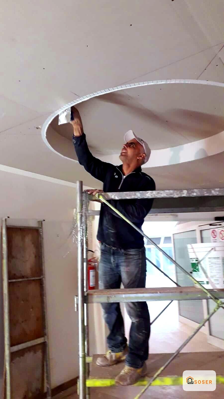 Operaio installa cartongesso su controsoffitto circolare in ambienti interni durante ristrutturazione