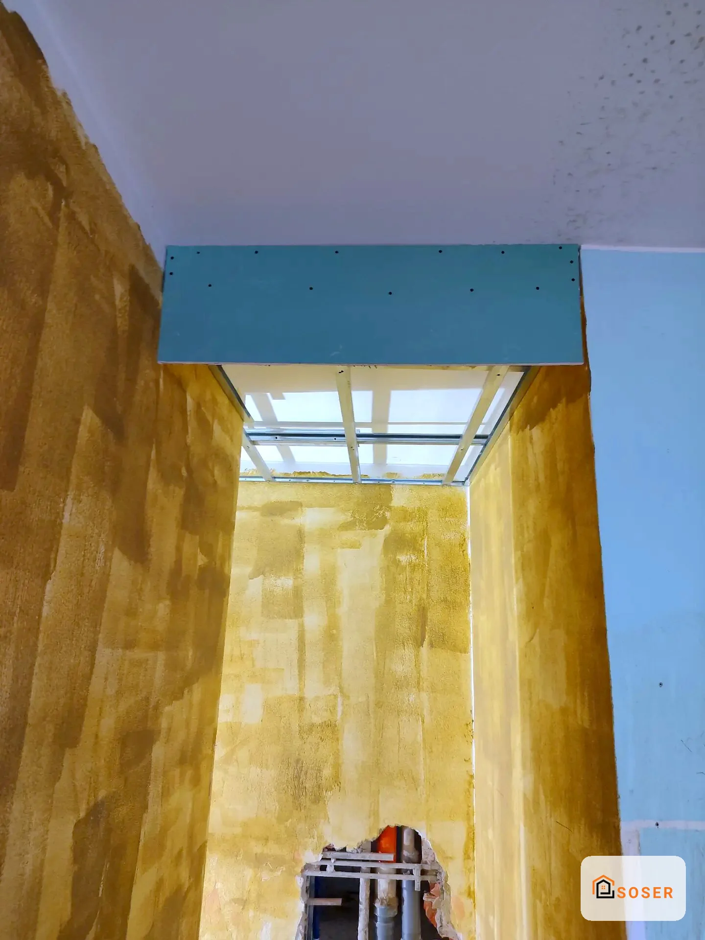 Interno di stanza in ristrutturazione con pareti intonacate in giallo e controsoffitto in cartongesso blu