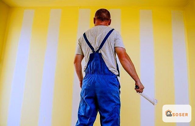 Operaio durante lavori di imbiancatura su parete a righe gialle e bianche