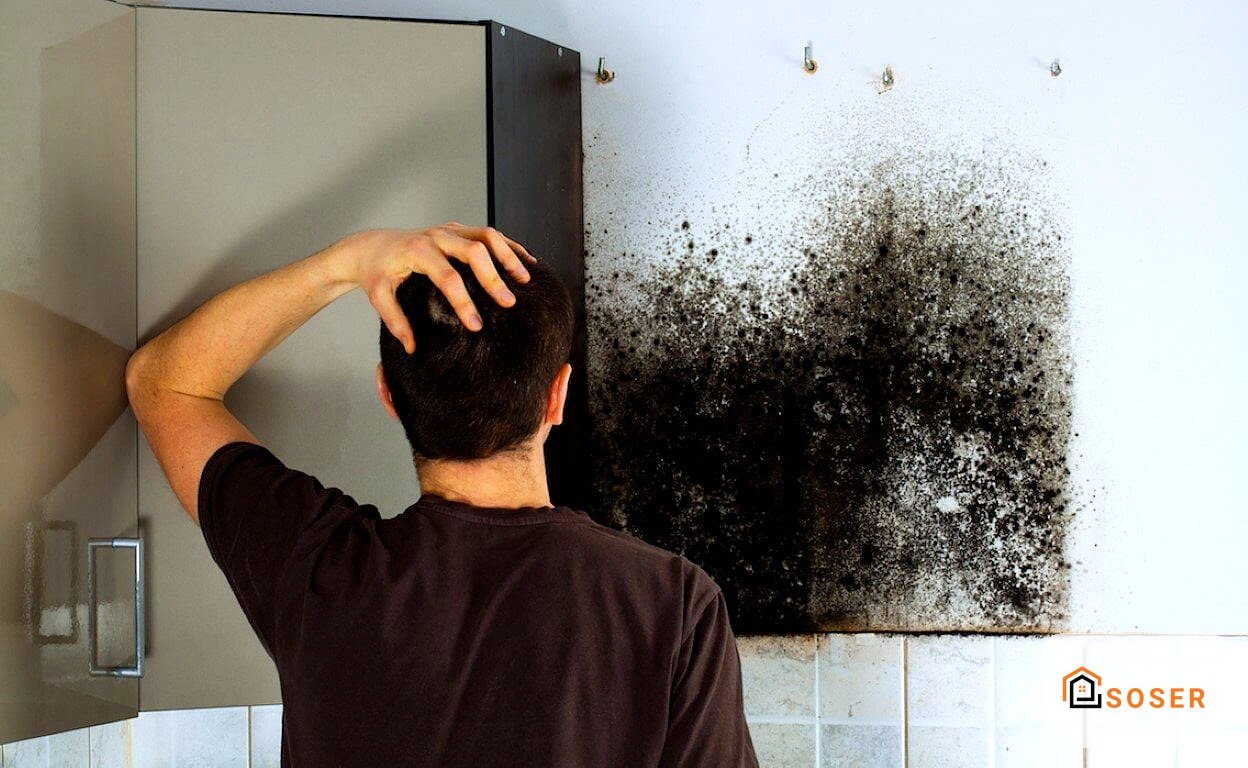 Uomo osserva muro bianco con macchie di muffa e umidità in bagno