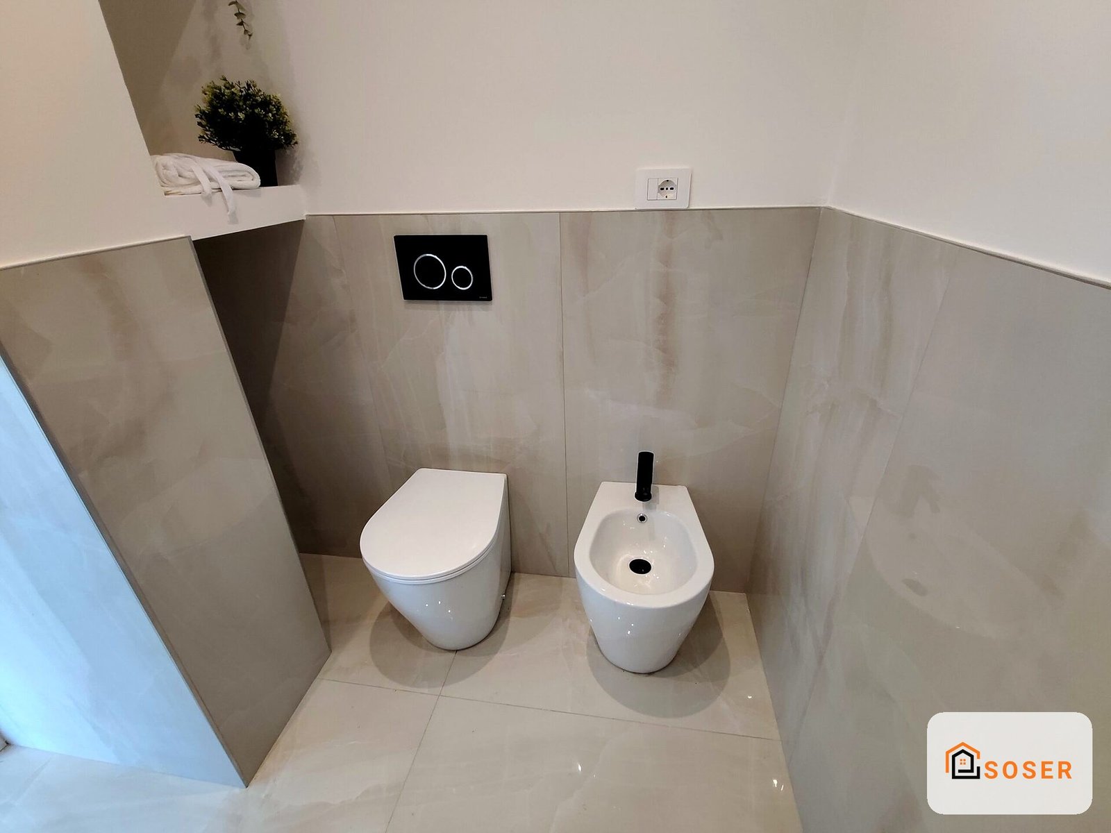 Bagno moderno con toilette e bidet bianchi, pareti in ceramica beige e finiture contemporanee