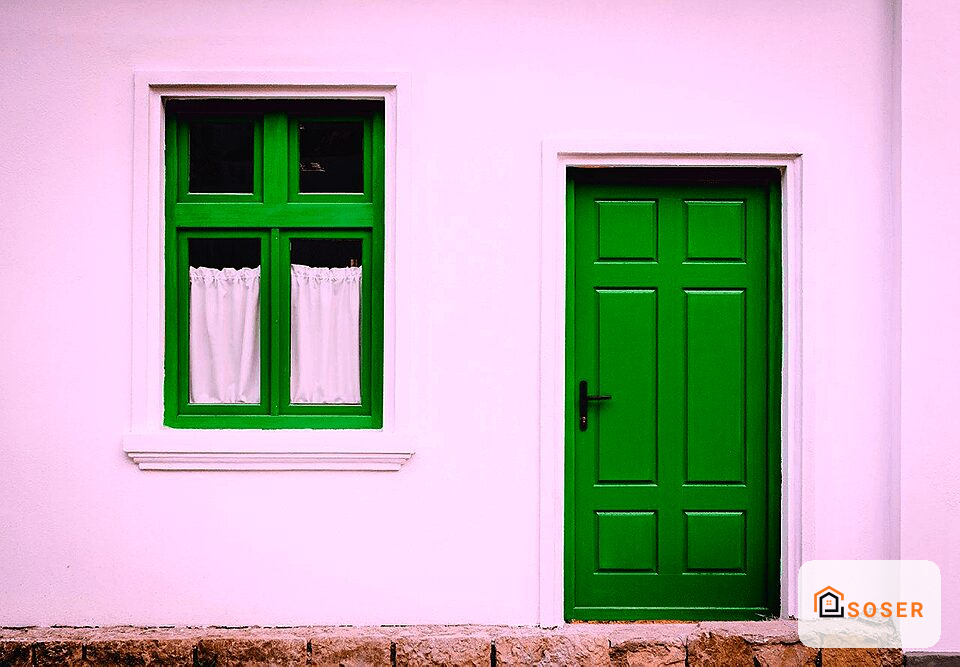Facciata di casa con parete rosa, finestra con infissi verdi e porta verde scuro