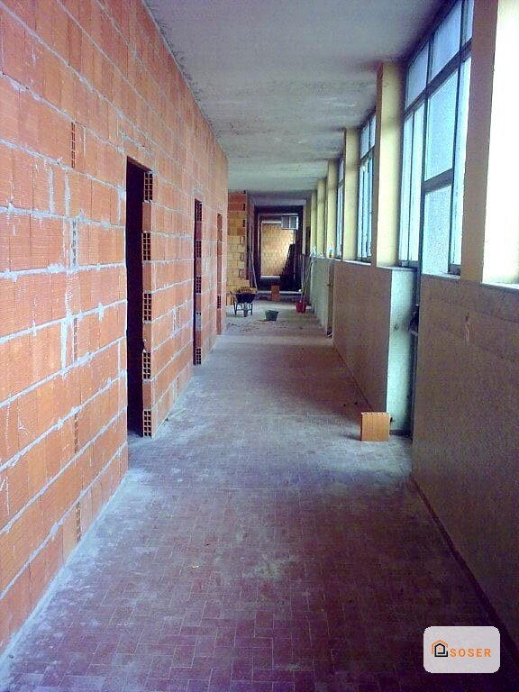 Corridoio in fase di ristrutturazione con pareti in laterizio rosso e pavimento grigio