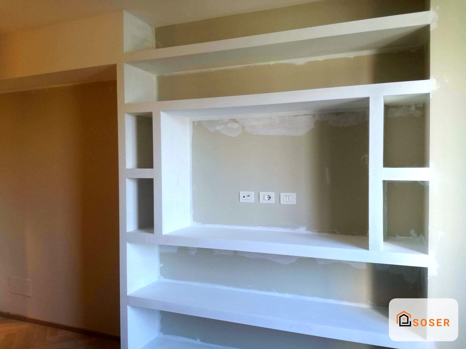 Libreria a muro in cartongesso bianco con vani aperti e ripiani, impianto elettrico visibile