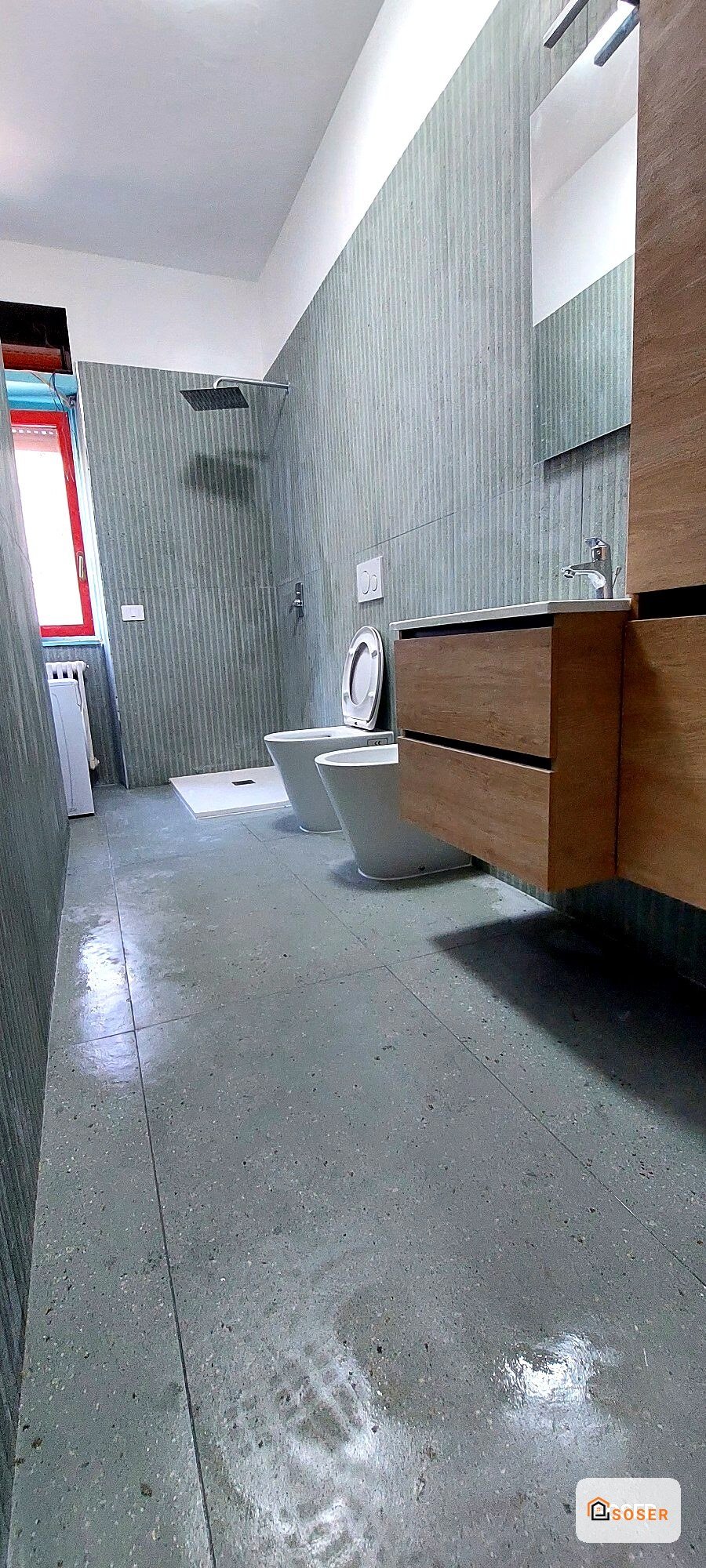Bagno moderno in ristrutturazione con piastrelle grigie, sanitari bianchi e mobile in legno