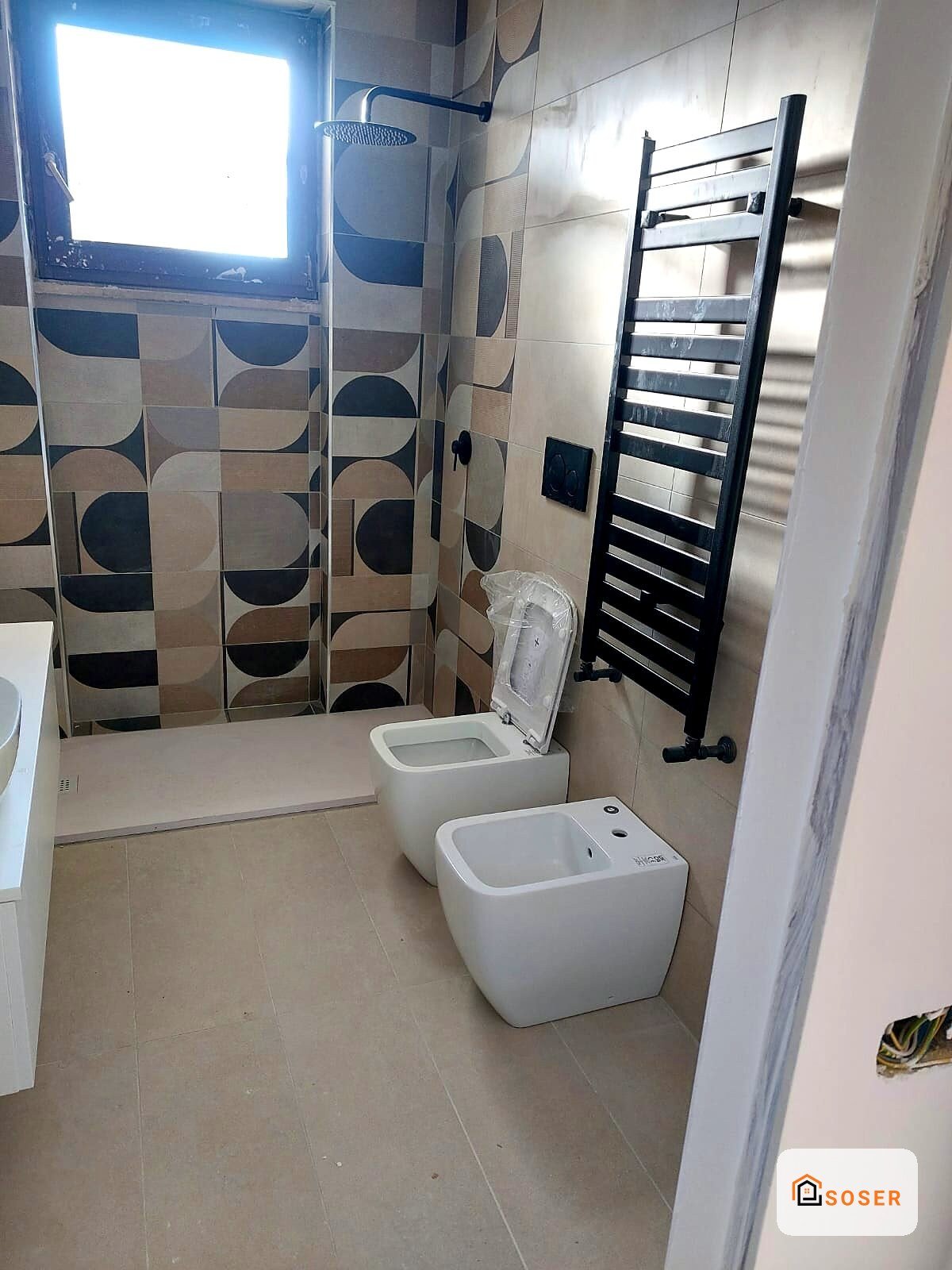 Bagno moderno in fase di ristrutturazione con sanitari bianchi, piastrelle geometriche e scaldasalviette nero